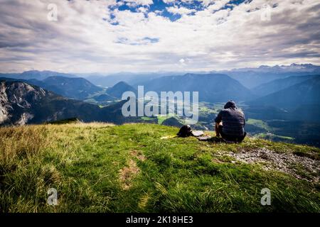 Un randonneur mâle, assis dans l'herbe, bénéficie d'une vue à couper le souffle depuis le sommet de la montagne du perdant, de l'Altaussee, de l'Ausser Land, du Salzkammergut, de la Styrie, Autriche Banque D'Images