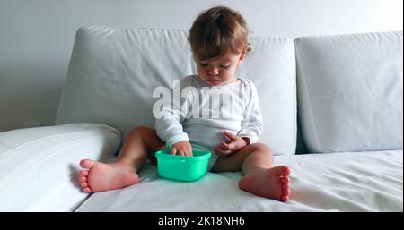 Bol de fin de nourriture pour bébé assis sur un canapé, mignon petit garçon d'un an Banque D'Images