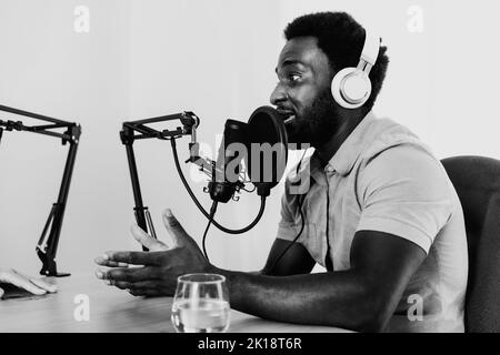 Homme africain enregistrant un podcast à l'aide d'un microphone et d'un casque de son studio personnel - montage noir et blanc Banque D'Images