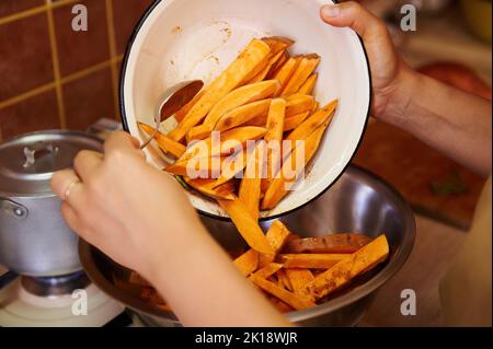 Concentration sélective sur des quartiers de patate douce bio dans un bol en émail dans les mains d'un cuisinier préparant un repas végétalien sain Banque D'Images