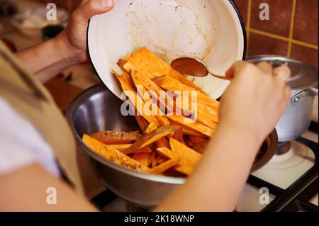 Concentrez-vous sur des tranches de batata bio saine dans un bol, dans les mains d'un chef cuisant un repas végétalien sain dans la cuisine maison Banque D'Images