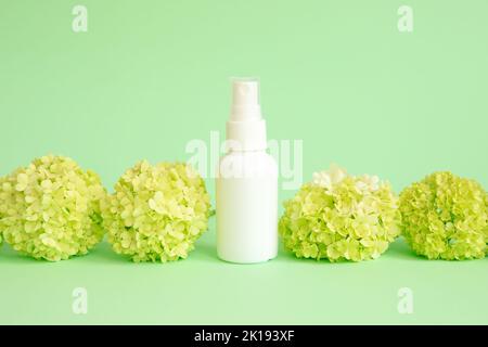 Vaporisateur cosmétique blanc et fleurs de viburnum vert sur fond vert. Vue de face, maquette, modèle. Cosmétiques naturels biologiques et fourmis liquide Banque D'Images