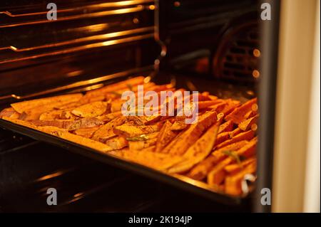 Gros plan de patates douces en tranches, des morceaux de batata sur une plaque de cuisson, cuits et frits avec des épices et des herbes dans le four Banque D'Images