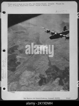 L'un des libérateurs du Consolidated B-24 de la US 8th AF quitte les gares ferroviaires à Aschaffenburg, en Allemagne, brûlant en arrière-plan alors que les heavies se dirigent vers la maison après des attaques réussies sur les communications nazies pour le septième consécutif Banque D'Images