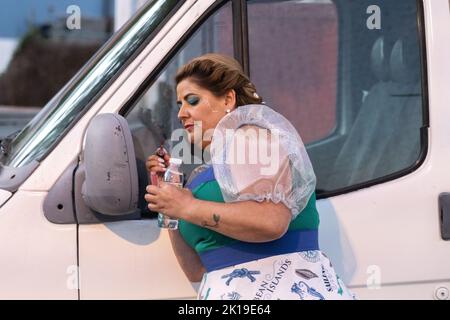 Un interprète costumé applique le maquillage de dernière minute à l'aide d'un miroir latéral de camion avant le début d'un défilé traditionnel de marcha au festival de Sanjoaninas, 23 juin 2022 à Angra do Heroísmo, île de Terceira, Açores, Portugal. Le festival marque la St John’s Day et est célébré par des défilés, des corridas et des activités culturelles. Banque D'Images