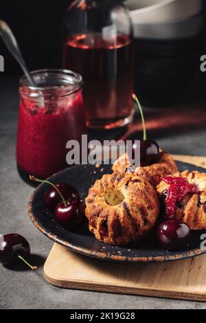 Petits gâteaux avec cerises sur fond sombre. Banque D'Images