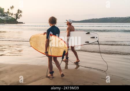 Père avec un fils adolescent avec planches de surf marchant sur une plage de sable sur l'océan sur l'île du Sri Lanka. Ils ont des vacances d'hiver et profiter d'un beau coucher de soleil Banque D'Images