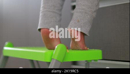 Bébé debout sur les tiptoes se tendre vers l'extérieur, mignon un enfant d'un an sur la petite chaise pointe-orteil Banque D'Images