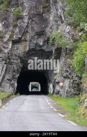 Kyrping, Norvège - 9 juin 2022: L'ancienne route du fjord d'Akra, POV d'un modèle Tesla 3 conduite sur la route pittoresque. Tunnel et ponts dans un ciel nuageux d Banque D'Images