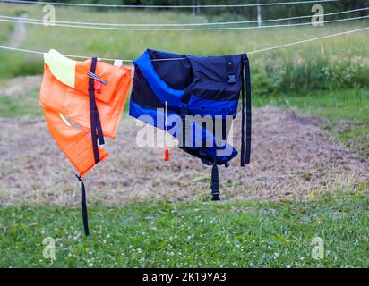 Gilets de sauvetage orange et bleu foncé séchant sur la corde à l'extérieur. Banque D'Images