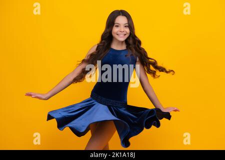 Visage de fille heureux, émotions positives et souriantes. Jeune adolescent gracieux enfant dans la mode robe isolée sur fond jaune. Robe de mouvement de jeune Banque D'Images