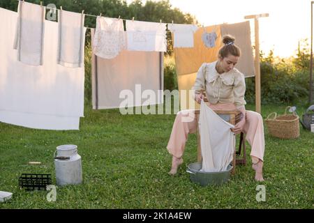 Jour de blanchisserie. Une femme porte du linge et des serviettes sur un arbre dans la cour d'une maison de village. Concept de chalet d'été. Banque D'Images