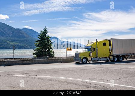 Américain jaune vif puissant vieux classique grand tracteur semi-remorque transportant des marchandises alimentaires dans réfrigérateur semi-remorque fonctionnant sur l'autoroute roa Banque D'Images