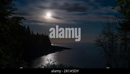 Rive nord du lac supérieur dans le Minnesota la nuit, avec reflet de la lune voilée obstruée par des nuages. Banque D'Images