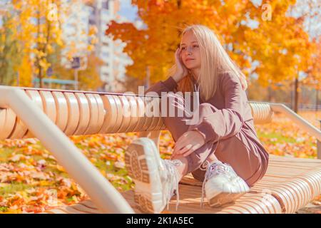 une adolescente est assise sur un banc sur le fond d'arbres jaunes d'automne.