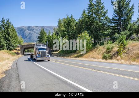 Tracteur semi-remorque blanc de style classique avec cabine allongée transport de semi-remorques à plateau vide fonctionnant sur la route divisée avec ar Banque D'Images