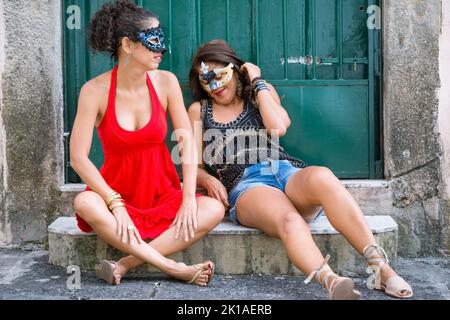 Portrait de deux belles et heureux filles assis contre une porte de couleur verte. Les filles de la ville loin de la capitale. Ils manipulent un masque de carnaval. Banque D'Images