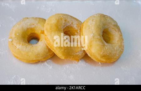 Frais cuits et garnis de beignets de sucre en poudre sur table blanche. Banque D'Images