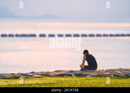 Une vue arrière de l'homme assis sur le rocher près du lac Banque D'Images