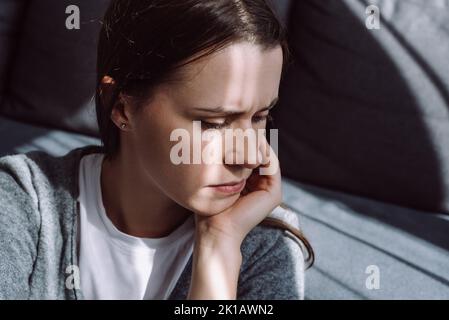 Concept de dépression. Portrait en gros plan d'une femme malheureuse et attentiste, assise seule sur un canapé à la maison, jeune frustrée et pensive Banque D'Images