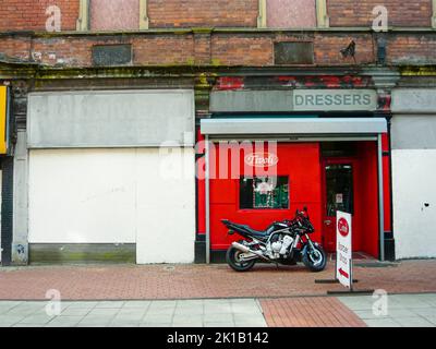 Une moto est garée devant un salon de coiffure dans une rue délabrée de Belfast. Banque D'Images