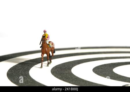 Photographie miniature de personnage de jouet de personnes. Des hommes jockey à cheval sur une piste de course depuis un dartboard. Isolé sur fond blanc. Photo d'image Banque D'Images