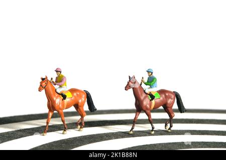 Photographie miniature de personnage de jouet de personnes. Des hommes jockey à cheval sur une piste de course depuis un dartboard. Isolé sur fond blanc. Photo d'image Banque D'Images