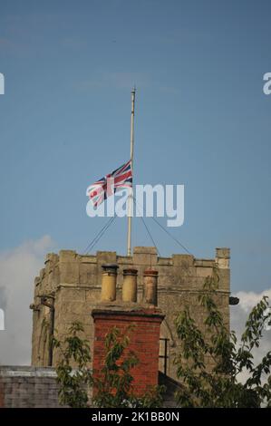 Église avec drapeau moitié mât Reine Elizabeth mort. Bleu ciel ensoleillé d'été et gros plan de la tour de l'église et des pots de cheminée. Banque D'Images