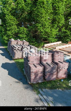 Vieux bardeaux de toit démontés après remplacement soigneusement empilés sur des palettes dans une lumière latérale ensoleillée avec des ombres. Banque D'Images