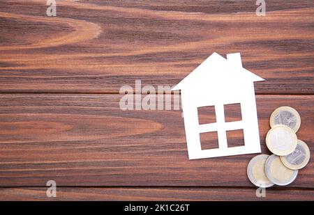 Maison en papier blanc avec pièces sur fond marron Banque D'Images