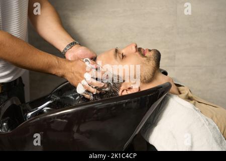 Jeune homme attrayant recevant un lavage de cheveux à la barbershop Banque D'Images