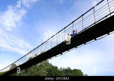 Homme assis sur le pont suspendu au-dessus de la rivière Belaya, Adygea Banque D'Images