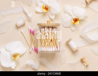 Coton bambou dans un pot près des fleurs d'orchidées blanches sur beige clair, vue du dessus. Produit de soin organique pour la peau pour la routine de beauté quotidienne. Bio écologique Banque D'Images