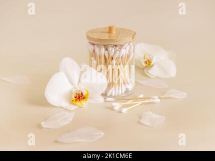 Le coton de bambou bourgeons dans un pot près des fleurs d'orchidées blanches sur beige clair, gros plan. Produit de soin organique pour la peau pour la routine de beauté quotidienne. Bio écologique Banque D'Images