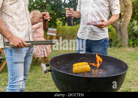 Cuisson au barbecue de maïs et de viande. Feu et fumée sur le gril et bière dans les mains. Banque D'Images