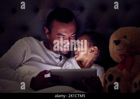 Père et enfant au lit avec un ebook de lecture de tablette ou de regarder un film ensemble la nuit. Bonne fille avec son père appréciant le film en direct en ligne Banque D'Images