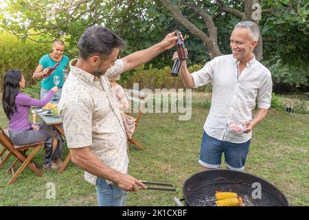 Groupe d'amis qui se sont mis à griller autour du barbecue. Des gens souriants buvant sur le patio. Banque D'Images