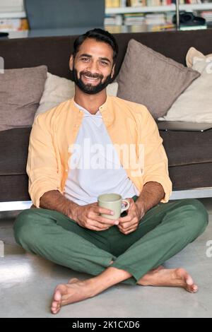 Un Indien heureux regardant l'appareil photo boire un café à la maison. Portrait vertical Banque D'Images