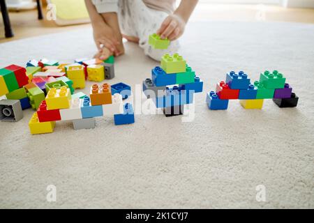 Un enfant joue des blocs de construction sur un tapis blanc. C'était la journée à la maison. Banque D'Images