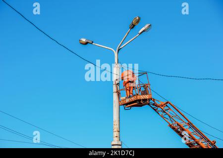 Un travailleur municipal en équipement de protection effectue des travaux dangereux pour éliminer une interruption du réseau électrique. Un employé répare une lampe de rue de Banque D'Images