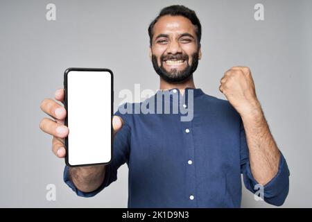 Un homme d'affaires indien heureux, isolé sur fond gris, montrant un téléphone mobile célébrant la victoire. Banque D'Images