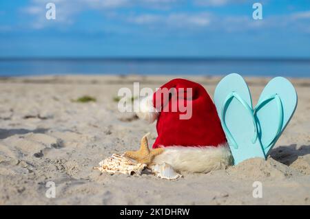 Fond de Noël chapeau de Père Noël sur la plage avec des étoiles de mer et des chaussons de plage Banque D'Images