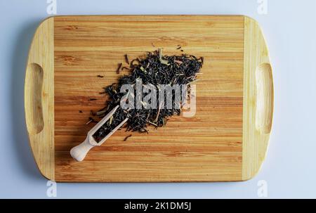 Le thé est prêt à être préparé. Spatule pour préparer le thé. Fond de feuilles de thé noir parfumées avec de l'herbe de citron. Thé sur une planche en bois. Banque D'Images