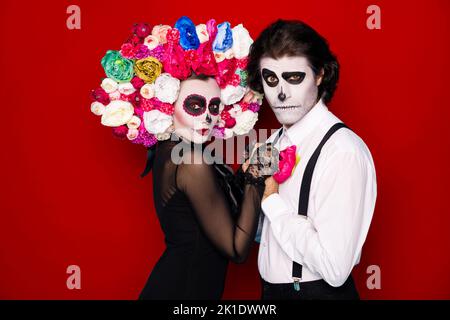 Photo de profil de couple effrayant homme fille femme mariée tenir mains danse passion tango porter robe noire tendance costume de mort décoration faciale, serre-tête roses Banque D'Images