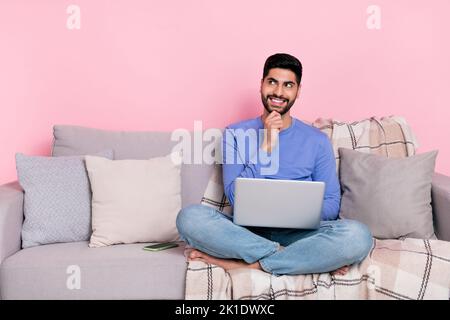 Photo d'un adorable garçon arabe vêtu d'un pull-over bleu assis avec un appareil moderne vide espace isolé couleur rose fond Banque D'Images