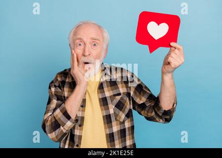 Photo de l'homme très impressionné retraité habillé damier chemise tenant le coeur comme signe bras joue isolé bleu couleur fond Banque D'Images