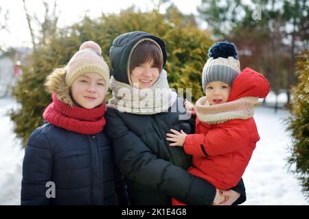 Deux jeunes sœurs mignonnes et leur petit frère s'amusent dans un parc couvert de neige le jour d'hiver. Enfants explorant la nature. Activités d'hiver Banque D'Images