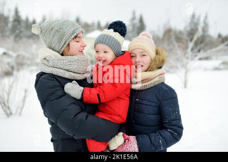 Deux jeunes sœurs mignonnes et leur petit frère s'amusent dans un parc couvert de neige le jour d'hiver. Enfants explorant la nature. Activités d'hiver Banque D'Images