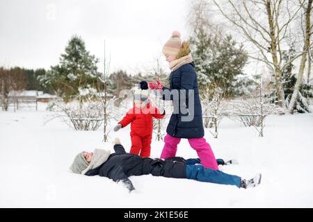 Deux jeunes sœurs mignonnes et leur petit frère s'amusent dans un parc couvert de neige le jour d'hiver. Enfants explorant la nature. Activités d'hiver Banque D'Images