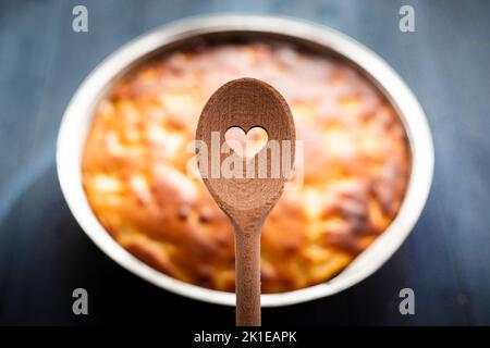 Cuillère en bois avec trou en forme de coeur, et tarte dans le fond sur table bleue. Concept cuit avec amour. Banque D'Images